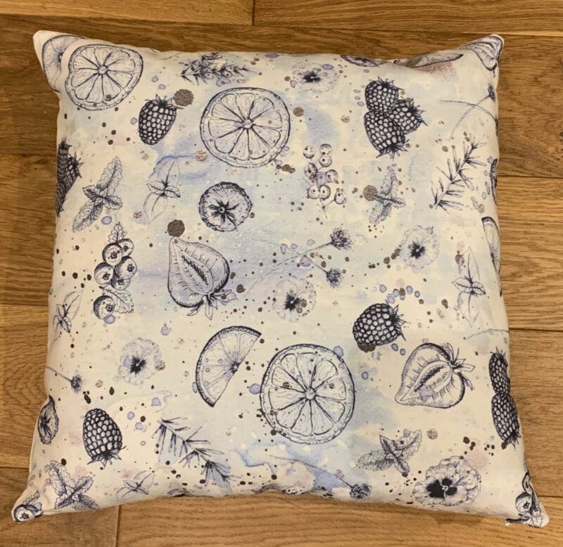A blue and white cushion with fruit and flowers on it.