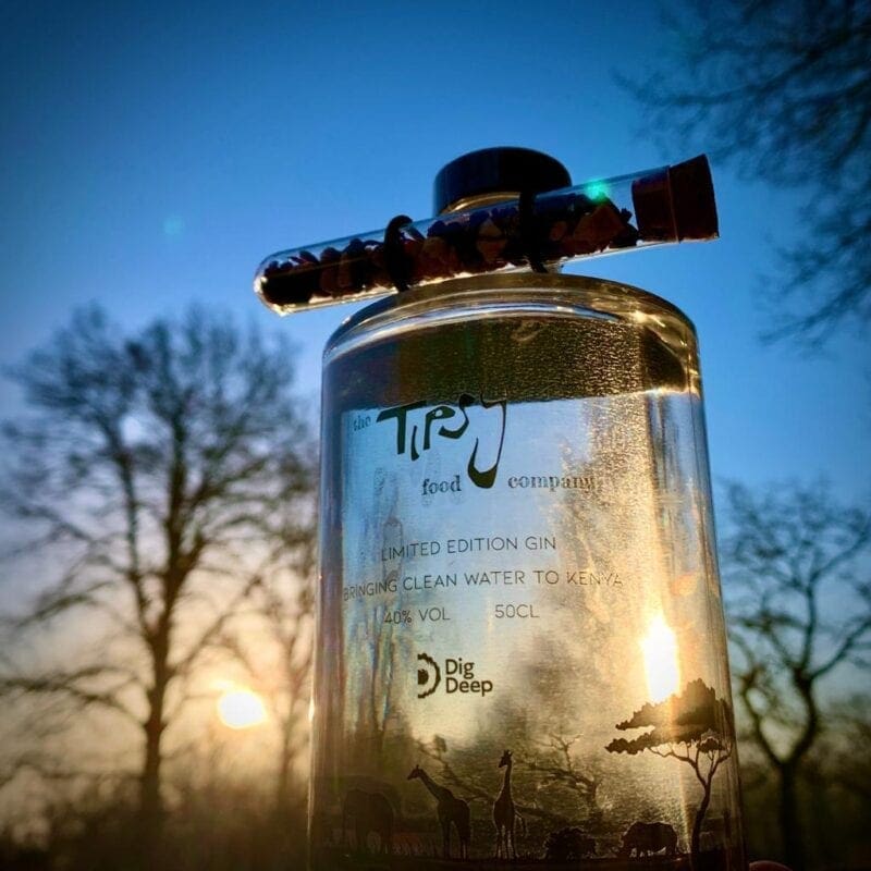 A person holds a bottle of East African Mango Gin (50cl) in front of a sunset.