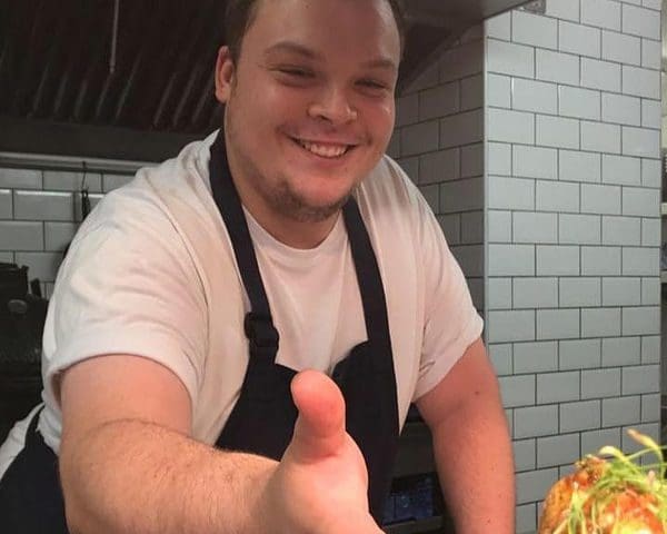A man in an apron is holding a plate of food.