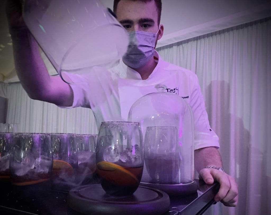 A chef wearing a mask pouring drinks into glasses.