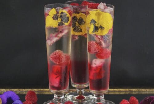 Three glasses with raspberries and pansies in them.