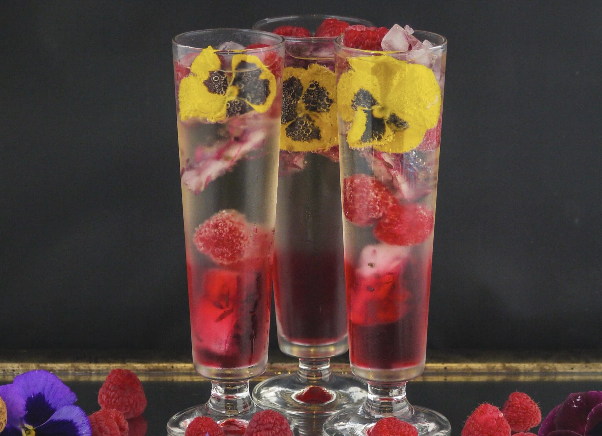 Three glasses with raspberries and pansies in them.