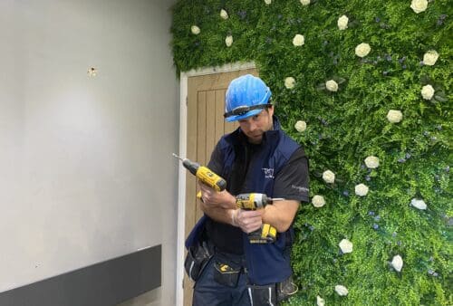 A man is holding a drill in front of a green wall.