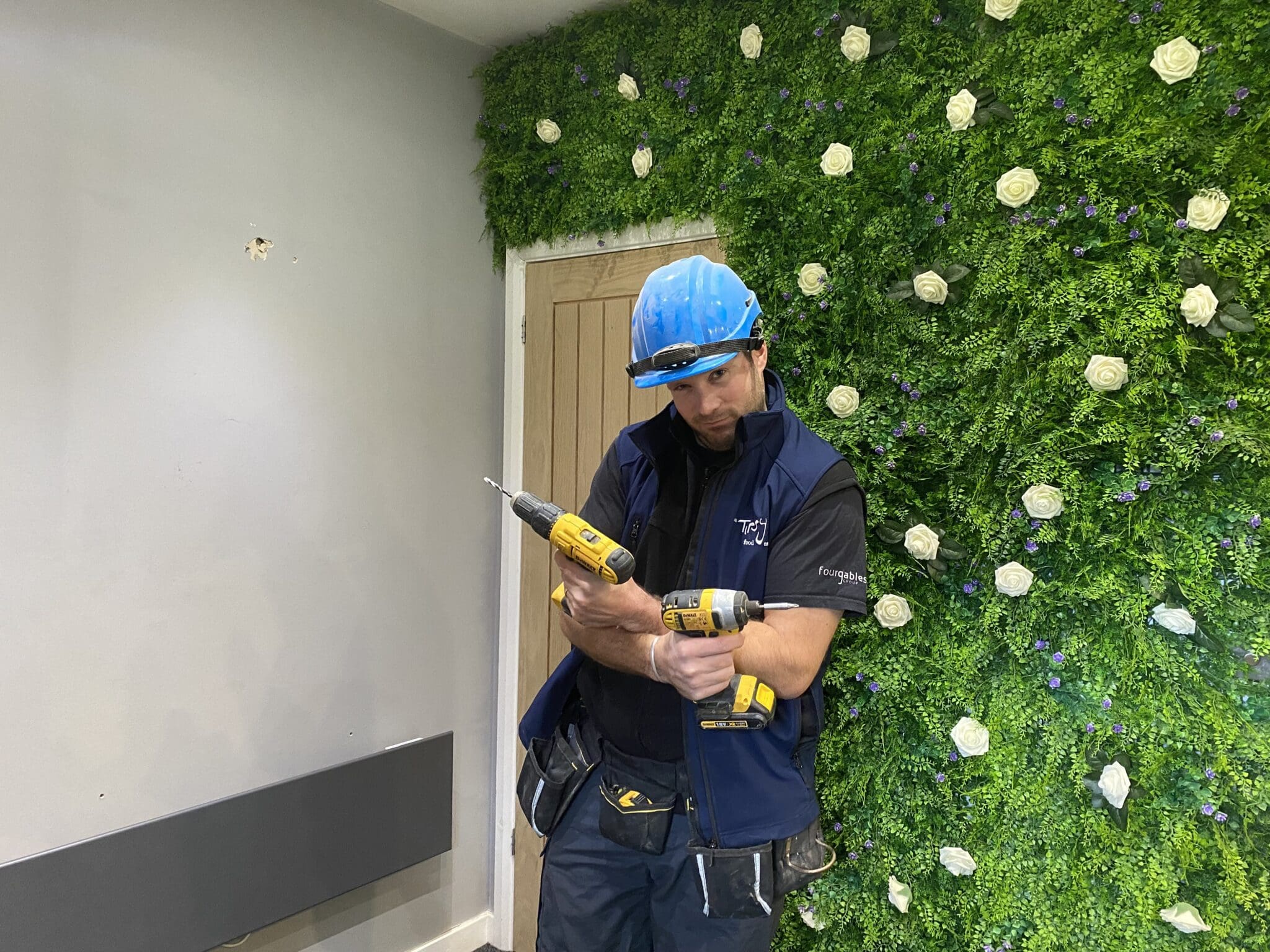 A man is holding a drill in front of a green wall.
