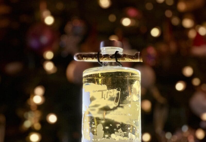A bottle of gin sitting on a table in front of a christmas tree.